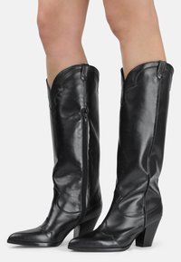 Botas de cuero negras hasta la rodilla con punta afilada, cierre de cremallera y costuras decorativas texturizadas a lo largo de los bordes y los lados.
