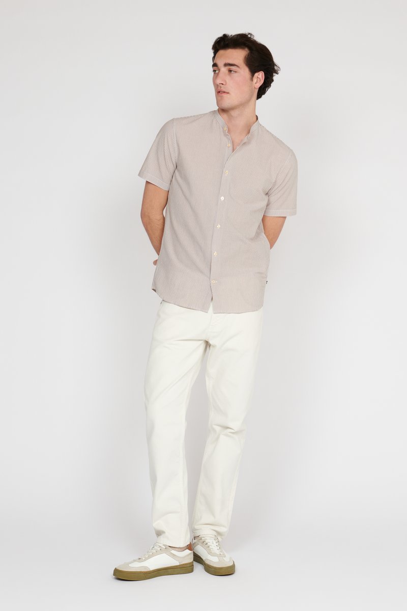 Kortarmige, knoopsluiting blouse met een licht beige en witte gestreepte patroon, gedragen met witte broek en sneakers met crème accenten.