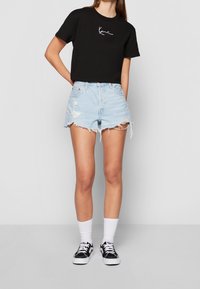 Svart kortärmad t-shirt med vit text, tillsammans med ljusblå slitna denimshorts. Svarta sneakers och vita sockor fulländar looken.