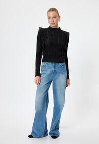 Maglione nero a maglia con motivo testurizzato e spalline arricciate, abbinato a jeans a gamba larga blu chiaro e scarpe nere.
