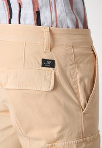 Beige katoenen shorts met een achterzak en een zwart label. Beschikken over een gladde textuur en een eenvoudig ontwerp, ontworpen voor comfort.