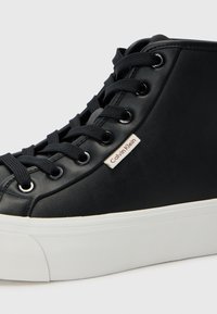 Sneakers neri alti realizzati in materiale liscia, con suola in gomma bianca, lacci neri e una piccola etichetta Calvin Klein sul lato.
