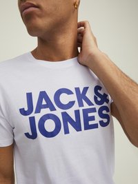 Bijela pamučna majica s masivnim plavim natpisom "JACK & JONES". Okrugli izrez i kratki rukavi. Mekana tekstura s opuštenim krojem.