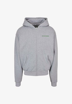 Szary rozpinany hoodie z miękkiego materiału, z przednią kieszenią, ściągaczami przy mankietach i dole oraz zielonym napisem na górze po lewej stronie klatki piersiowej.