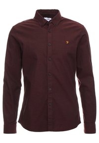 Camisa de manga larga y botones en color burdeos oscuro, con cuello abotonado y pequeño logo "F" bordado en amarillo en el pecho izquierdo.