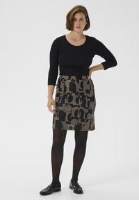 Schwarz langärmliges Oberteil kombiniert mit einem gemusterten beige-schwarzen Bleistiftrock, der abstrakte Formen aufweist. Schwarze Strumpfhosen und Loafers runden das Outfit ab.