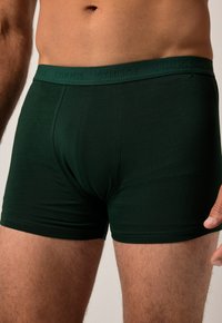 Shorts en coton vert foncé, dotés d'une taille douce avec une texture de marque et d'un design lisse et ajusté pour plus de confort.