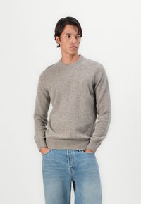 Sweater cinza claro feito de malha texturizada, com gola redonda e punhos canelados. Combinado com jeans de denim azul claro.