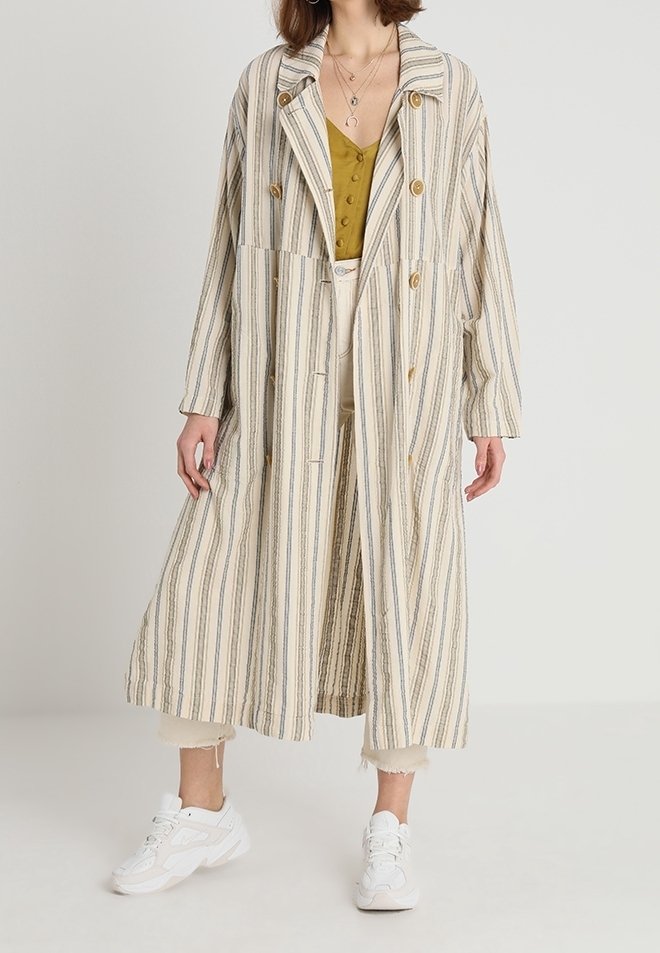 Pruhovaný dlouhý kabát v béžové, modré a krémové barvě. Má vykrojený límec, dvouřadé zapínání a velké knoflíky. Nosený přes hořčicový top.