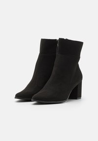 Botas de tobillo de ante negro con punta afilada y tacón grueso, que cuentan con una cremallera lateral y una textura suave.