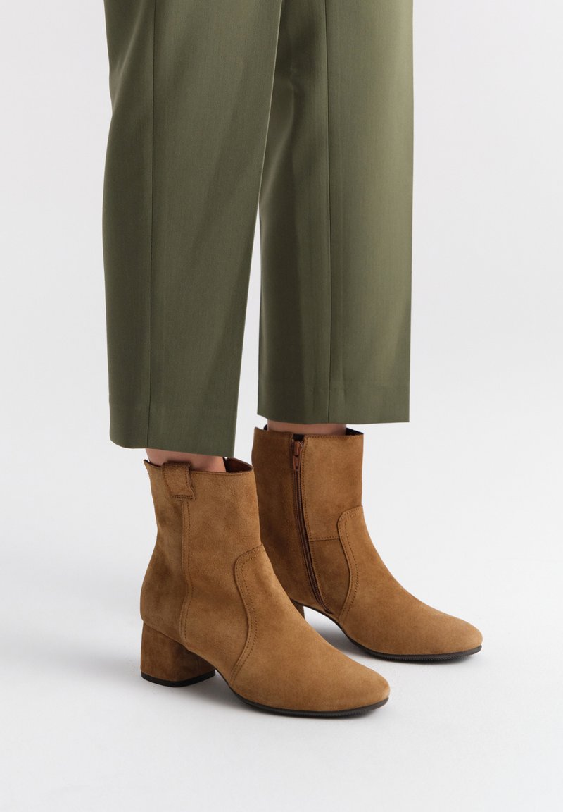 Brązowe zamszowe botki za kostkę na słupku, z bocznym zamkiem błyskawicznym, spiczastym noskiem i gładką teksturą, w połączeniu z oliwkowymi spodniami.