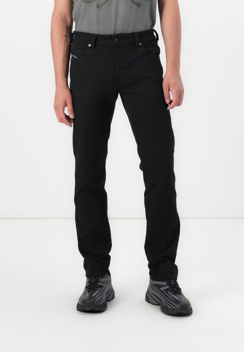 Mustad denim teksased aluspüksid, millel on slim fit lõige, klassikaline viie tasku disain, eristuvad õmblused ja tõmblukk. Stiliseeritud halli T-särgiga ja mustade tossudega.