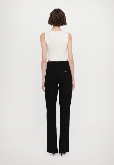 White sleeveless top with a back zipper, paired with high-waisted black jeans featuring a gold logo accent on the back pocket.