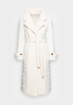 Lungo cappotto invernale imbottito bianco con collo a rever in pelliccia, cintura abbinata e polsini con bottoni su sfondo neutro.
