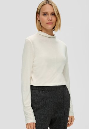 Langsleeve ivoorkleurig top met een hoge halslijn, met een gladde textuur en een subtiele naaddetail, gecombineerd met donkere, gestructureerde broeken.