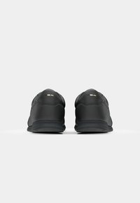 Sapatilhas atléticas pretas com um cabedal sintético suave, colarinho acolchoado e sola de borracha com um padrão de piso. Detalhes de destaque sutis.