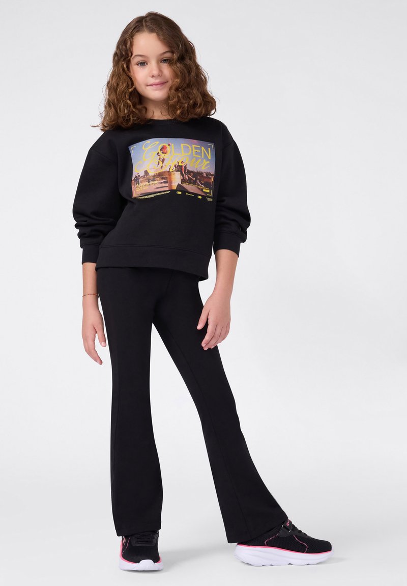 Zwarte sweatshirt met een kleurraf grafiek, gecombineerd met zwarte flare-broeken. G gedragen met zwarte sneakers met roze accenten.