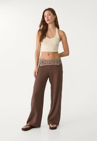 Krämfärgad virkad cropped topp med vida bruna ribbade byxor med mönstrad midjeresår. Sandaler fulländar den avslappnade outfiten.