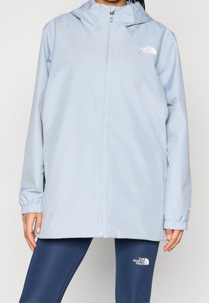 Person iført en lyseblå hættejakke med lynlås og mørkeblå leggings, begge med The North Face-logo.