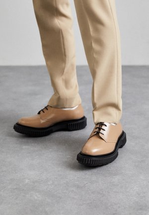 Lichtbruine leren schoenen met een ronde neus, zwarte rubberen zool, vetersluiting en stiksels, gecombineerd met beige broek.