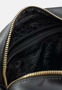 Musta nahkabagi sisemus kuldse tõmbelukuga, mitmete taskutega, tekstuuriga voodriga ja diskreetse geomeetrilise mustriga.