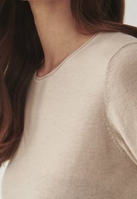 Lichtbeige, aansluitende gebreide trui met een ronde halslijn en delicate steekdetails langs de schouders en naden. Zachte textuur.