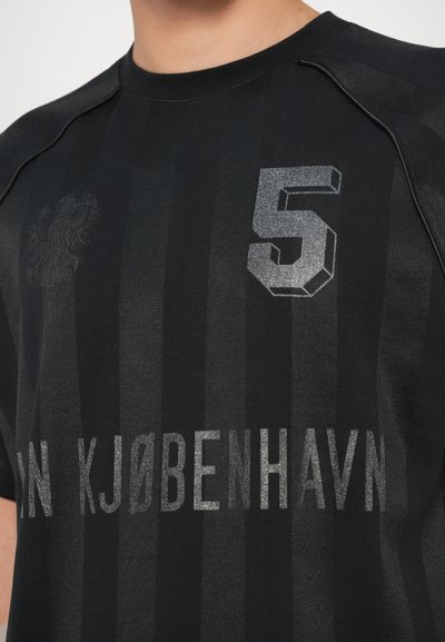 Melns sporta krekls ar horizontālām svītrām, sudraba "5" un tekstu "IN KØBENHAVN" izteiksmīgā fontā. Gluda auduma ar apaļu kakla izgriezumu.