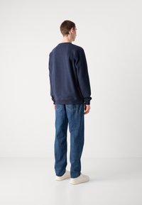 Navy sweatshirt with long sleeves and ribbed cuffs, paired with light blue loose-fitting jeans and white sneakers. Simple design, no patterns.