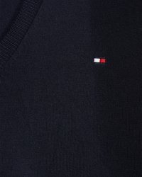 Tmavě modrá pletená vesta s výstřihem do V, která má malé logo s červenými, bílými a modrými akcenty umístěné na levé straně.