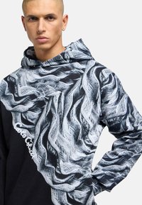 Black hoodie featuring a textured gray and white abstract pattern, with a kangaroo pocket and an embroidered logo on the front.