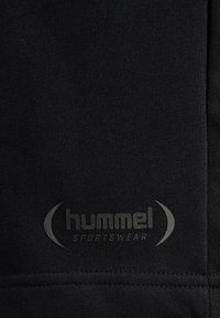 Schwarzer Sportstoff mit strukturierter Oberfläche, mit dem Logo "hummel" und "SPORTSWEAR" in Grau, nahe dem unteren Rand platziert.