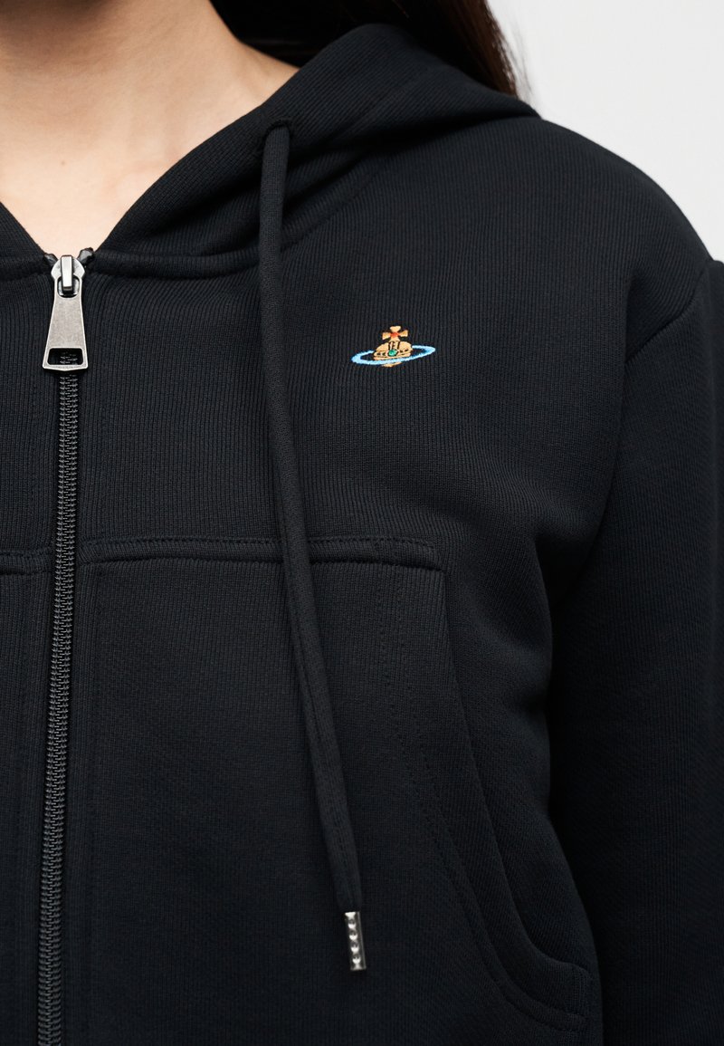 Sweat à capuche noir zippé en tissu côtelé. Comprend une poche avant et un motif brodé sur la poitrine. Fermeture éclair et cordons argentés.