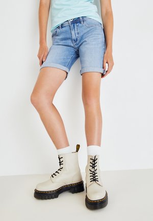 Shorts en denim bleu clair avec des ourlets retroussés associés à des bottines beige à lacets avec une semelle épaisse noire et des accents de couture jaunes.