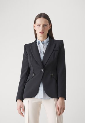 Blazer nero su misura con design doppiopetto, due bottoni, rever affilati e spalle strutturate, indossato sopra una camicia azzurro chiaro.
