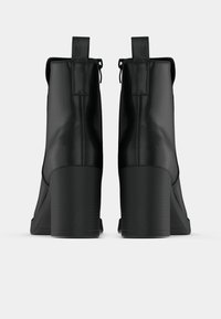 Bottines noires à fini brillant, talons carrés hauts et languettes à l'arrière ; présentent une texture lisse et un design minimaliste.