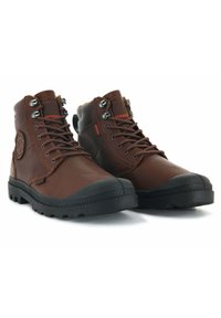 Botas de senderismo de cuero marrón con paneles texturizados, punteras de goma negra y herrajes de metal. Presenta un etiquetado impermeable y suelas resistentes.
