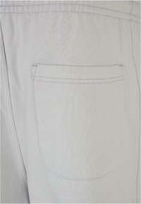 Helle graue Jogginghosen mit strukturiertem Finish, ausgestattet mit einer Rückentasche, die mit passender Naht umrandet ist. Weicher Stoff und elastischer Bund.