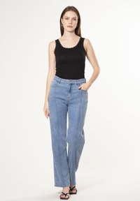 Top de tirantes negro con forma de ola, vaqueros de pierna ancha en azul claro con costuras frontales y sandalias negras de tiras; tejido suave y corte relajado.