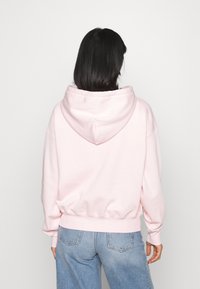 Ljusrosa hoodie i mjukt tyg, med en framficka, dragsko i huvan och ribbade ärmslut. Kombineras med blå jeans.