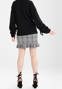 Svart långärmad topp med sidoknutar, ihop med en grårutig minikjol med volangkant. Svarta ankelbandsklackar fulländar looken.