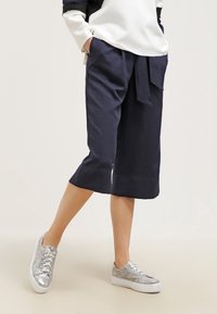 Krajkové kalhoty v námořnické modři, vyrobené z lnu, s vázáním v pase a širokými nohavicemi. V kombinaci se stříbrnými metalickými teniskami.