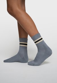 Chaussettes côtelées grises avec deux bandes horizontales en crème et noir au niveau du bord-côte. Texture douce et longueur standard à la cheville.