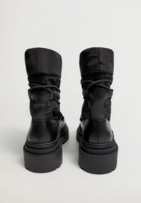 Bottes noires à la cheville avec une tige en cuir lisse et textile rembourré, dotées d'une semelle en caoutchouc épaisse et de détails de laçage ajustables.