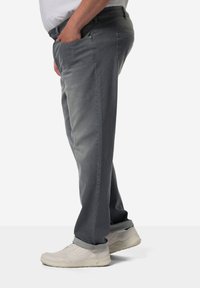 Ljust grå jeans sedd från sidan, med rak passform, fickor och uppvikta muddar, tillsammans med vita sneakers.
