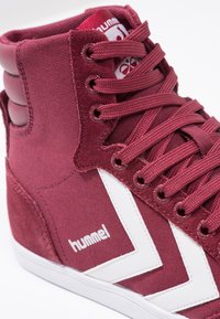 Tenisi înalți din pânză burgundy cu design în formă de v cu alb, șireturi rotunde și accente de suede texturat. Logo-ul este afișat pe lateral.