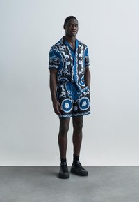 Modrá košile s krátkými rukávy a odpovídající šortky s složitými černobílými vzory. Vyrobeno z lehké tkaniny, má volný střih.