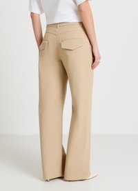 Pantalon beige à jambes larges en tissu texturé, avec deux poches arrière plates et une taille haute, vu de dos.