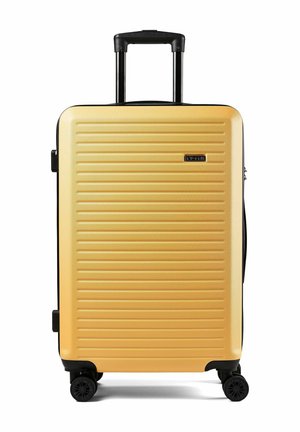 Valigia rigida gialla con scanalature orizzontali, manico nero retraibile, quattro ruote nere girevoli e maniglie laterali.