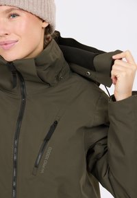 Oliivivihreä vedenpitävä takki, jossa on korkea kaulus, etuvetoketju, sivuvetoketjullinen tasku ja säädettävä kaula-aukko. Ominaisuuksiin kuuluu W.PRO 10000 -brändäys.