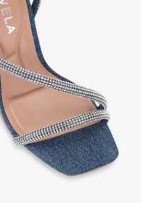 Dżinsowe sandały na wysokim obcasie z kwadratowym noskiem, z dwiema skośnymi paskami ozdobionymi przezroczystymi cyrkoniami i beżową wkładką.
